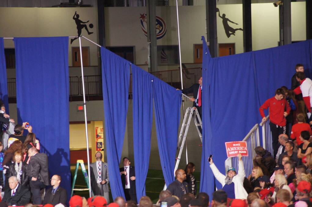 Team Trump rush to repair a collapsed curtain at the back of the stage.
